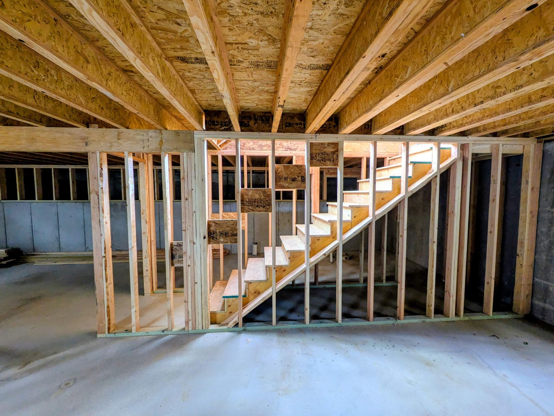 Framed walls and an open wooden stair under floor joists.