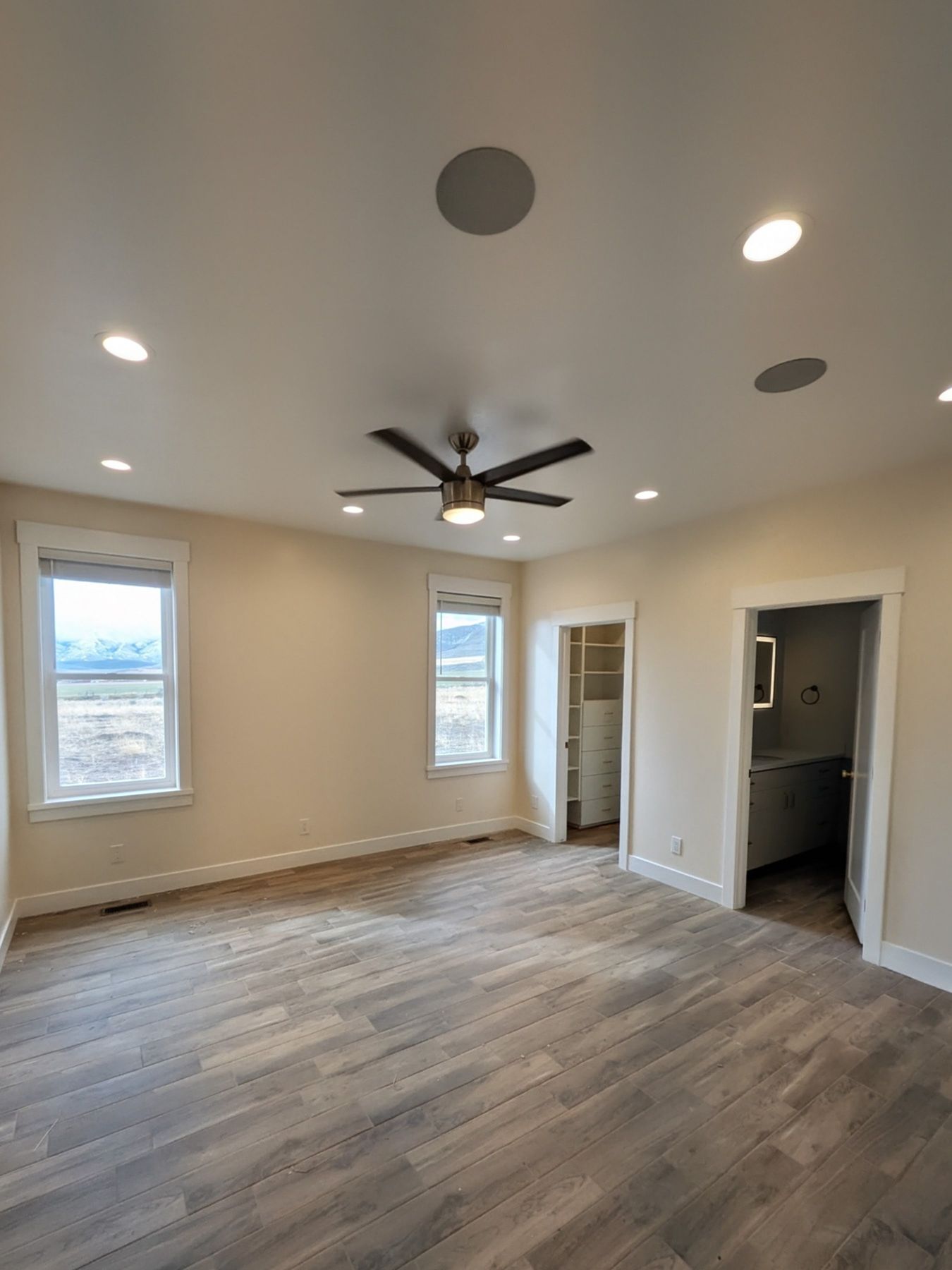 Bright bedroom with plank flooring, ceiling fan and recessed lights.