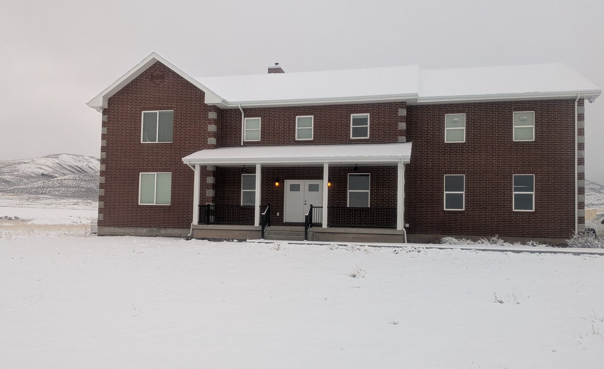 Two-story brick home with a white covered porch after a snowfall.