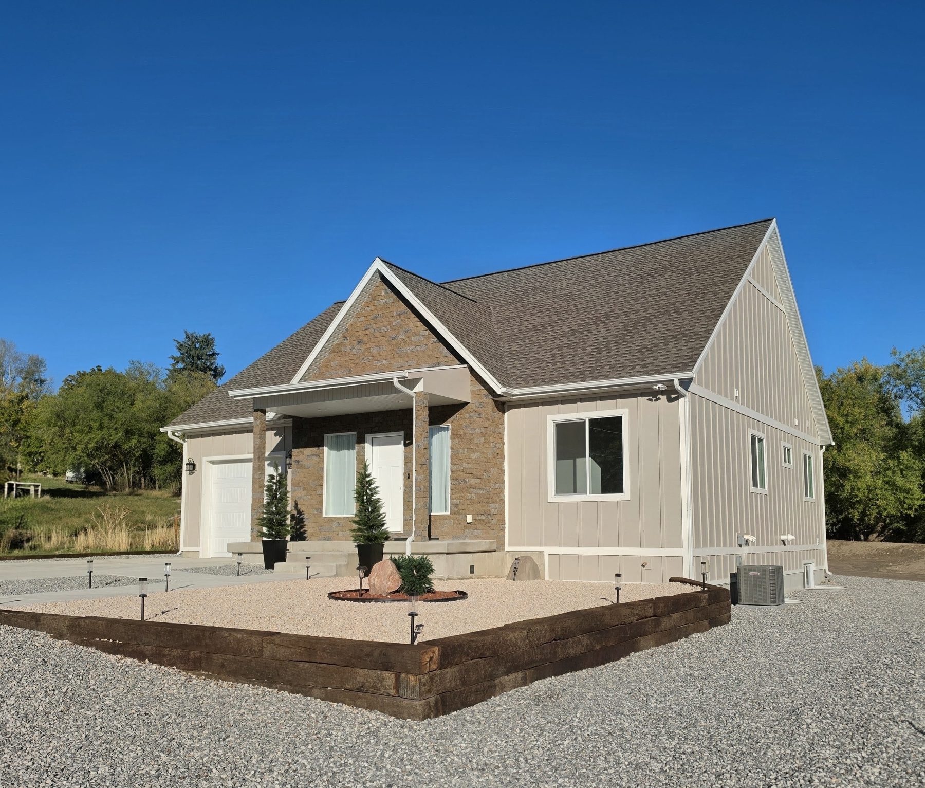 Finished single-story home with stone and board-and-batten siding, a timber-framed porch and new landscaping.