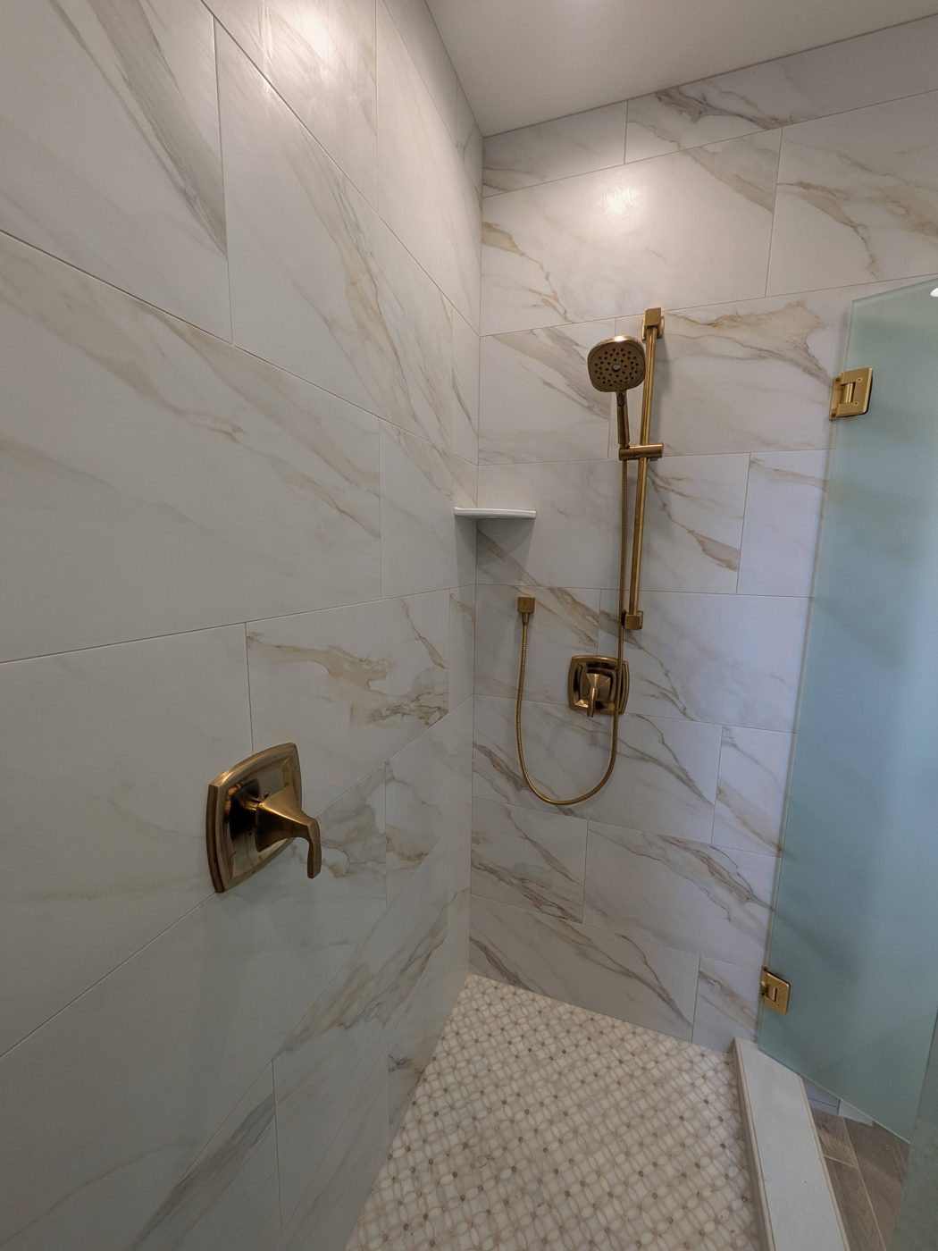Shower wall with marble-look tile and brushed brass fixtures.
