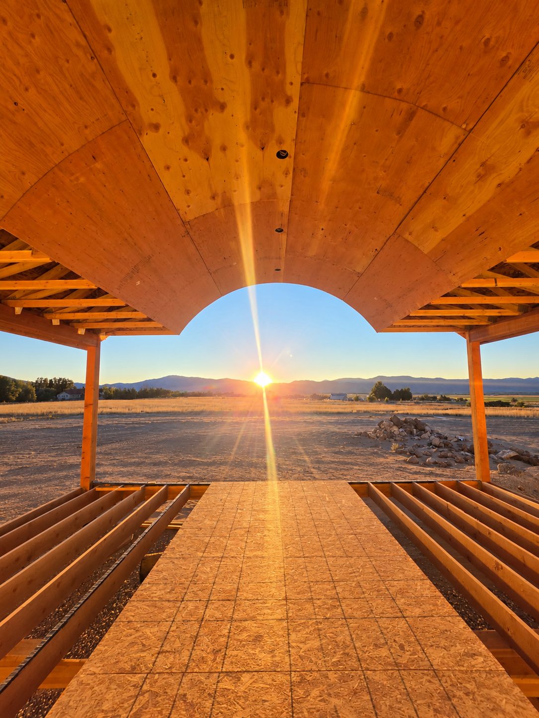 Looking out from under a timber pavilion roof toward a valley at sunset.